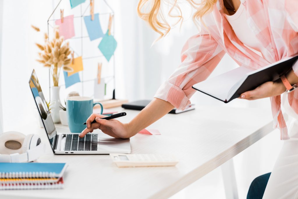Woman blogging on her computer with a notebook and her notes